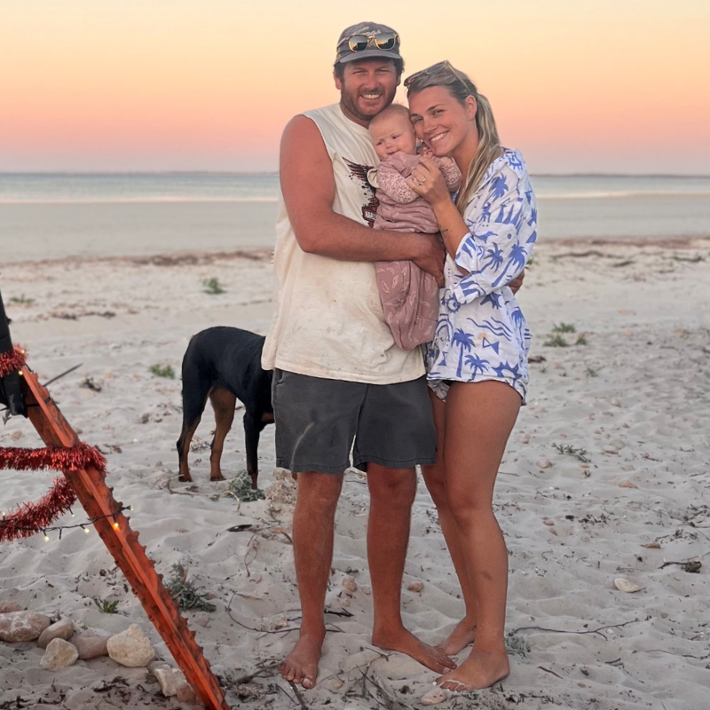 Family standing on a beach at sunset holding a baby with a dog nearby
