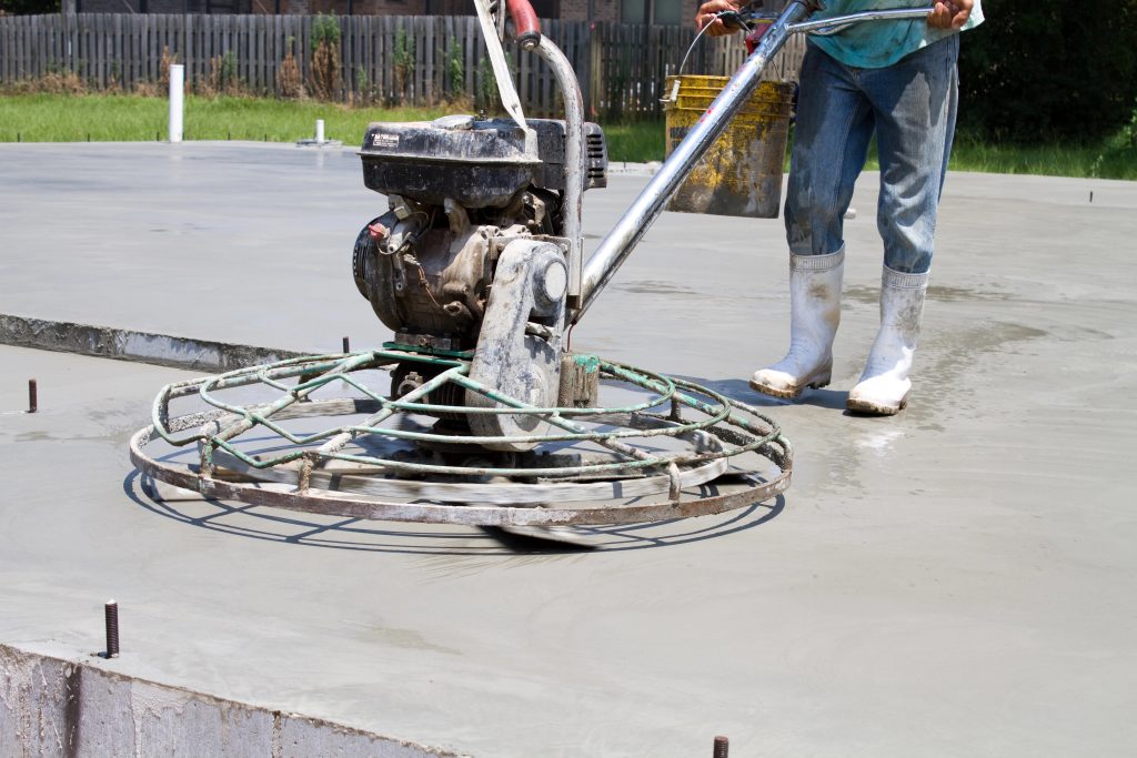 Concreter finishing a freshly poured concrete slab using a power trowel machine