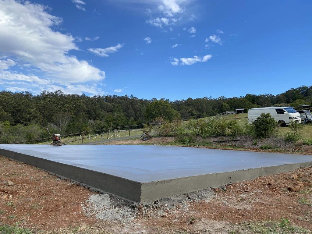 Freshly poured 12m x 12m concrete shed slab on a rural acreage block with power trowel at the edge