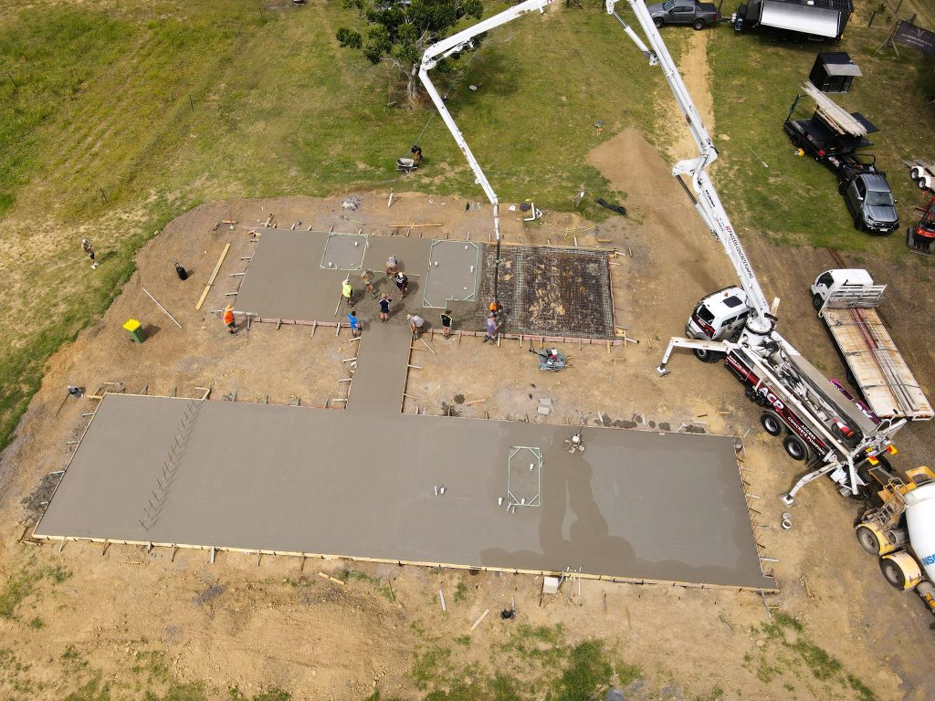 Aerial view of a large house slab pour with concrete pump truck and crew working across the formed sections
