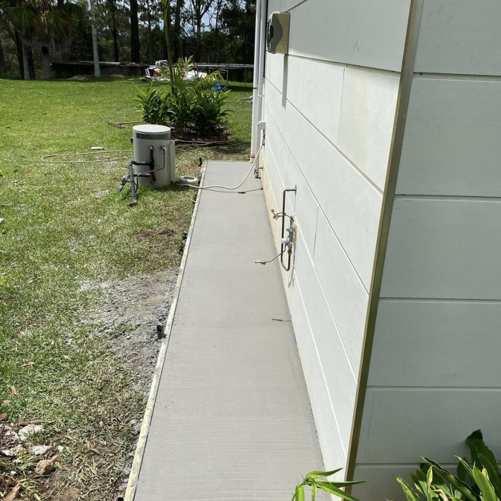 Newly poured concrete footpath running along the side of a weatherboard house beside a grassed yard