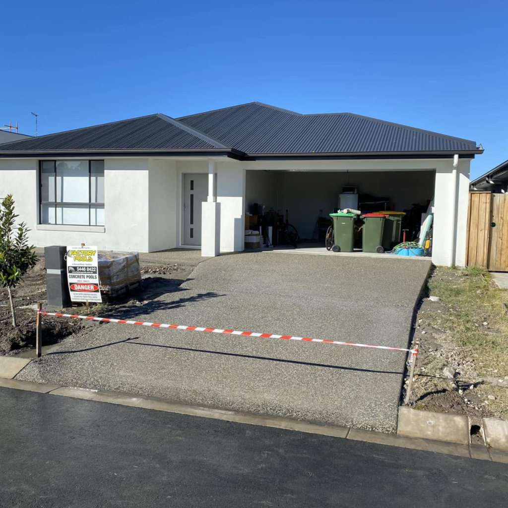 Exposed aggregate concrete driveway leading to the garage of a modern Sunshine Coast home, taped off while curing